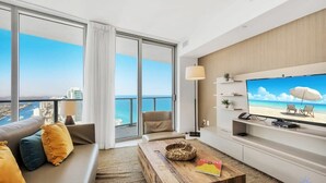 A modern living room with a large TV, a sofa, a coffee table, and a view of the ocean. - Insane Ocean View Balcony| Beachfront Resort+ Gym (Hollywood)
