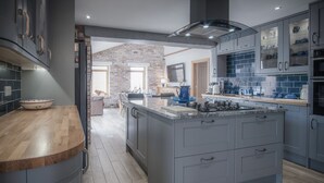 A modern kitchen with grey cabinetry, a large island, and a brick wall. - Bayview House - 4 Bedroom - Saundersfoot (Saundersfoot)