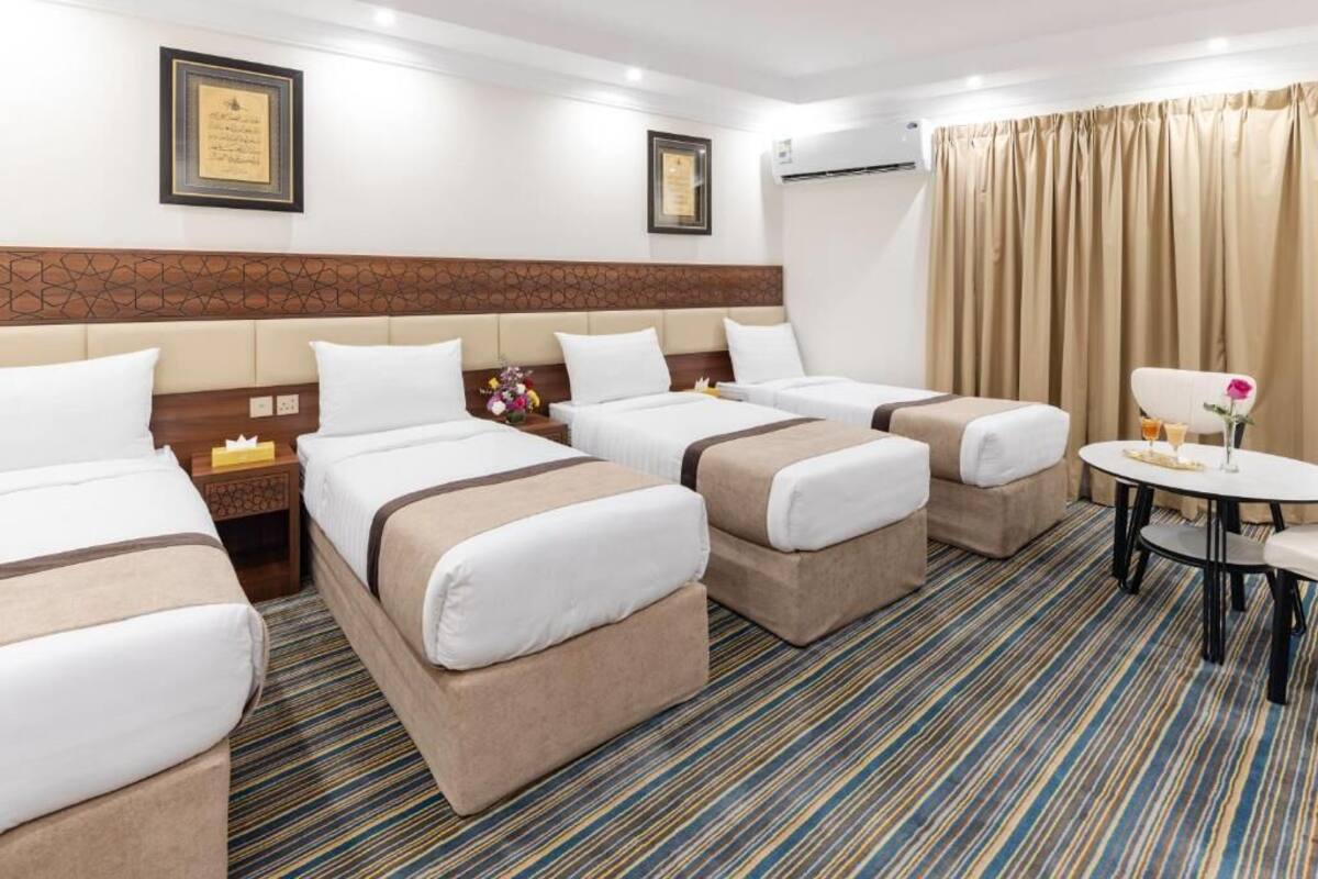 Una habitación de hotel con tres camas, una mesita y una cortina.
