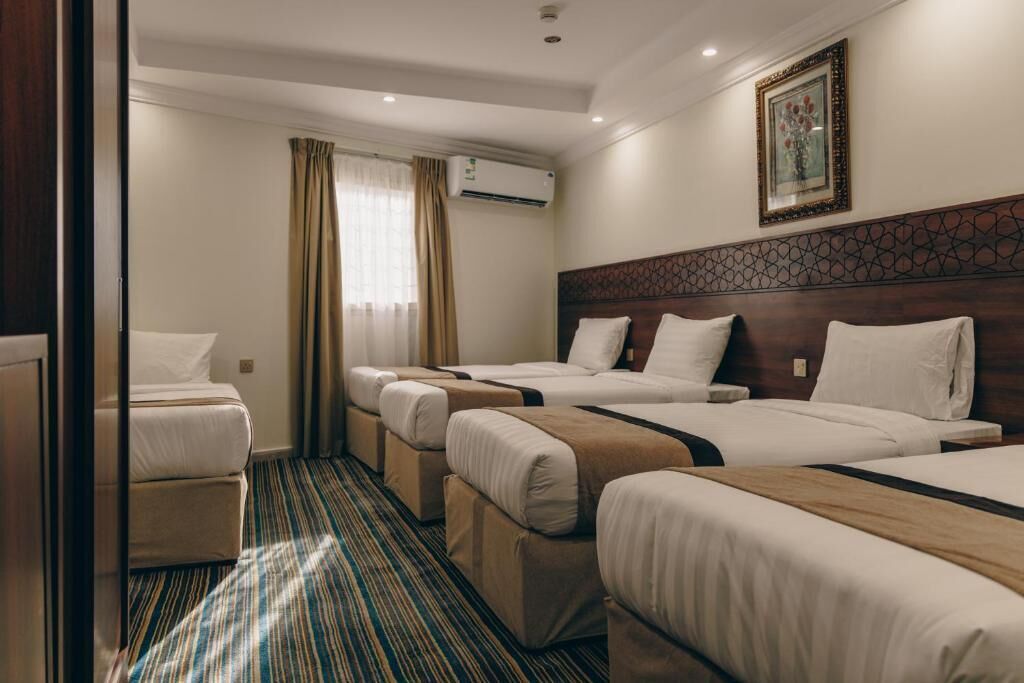 Habitación de hotel con tres camas, una ventana con cortinas, un equipo de aire acondicionado y un cuadro en la pared.