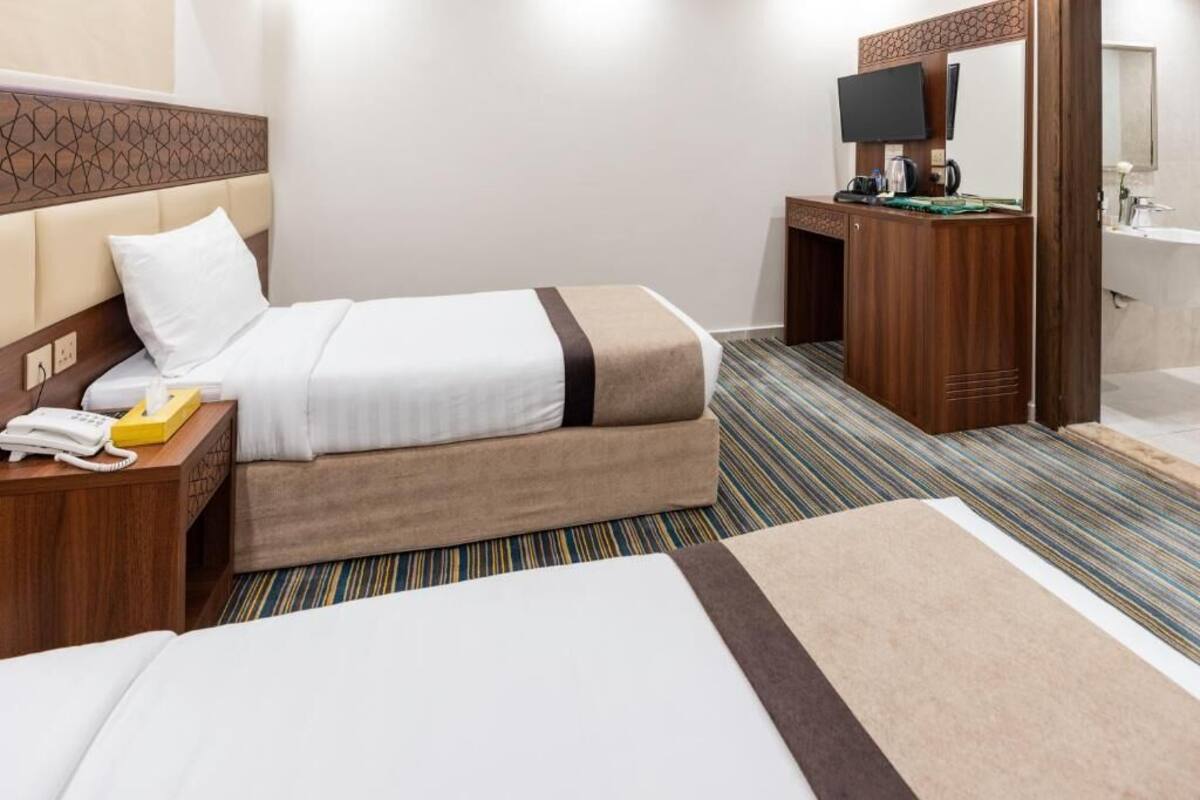 Habitación de hotel con cama, mesita de noche con teléfono, televisión y baño con espejo y lavamanos.