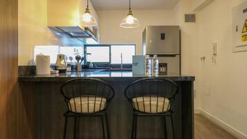 A modern kitchen with a central island, two bar stools, pendant lighting, a stainless steel refrigerator, and a view of the outside.