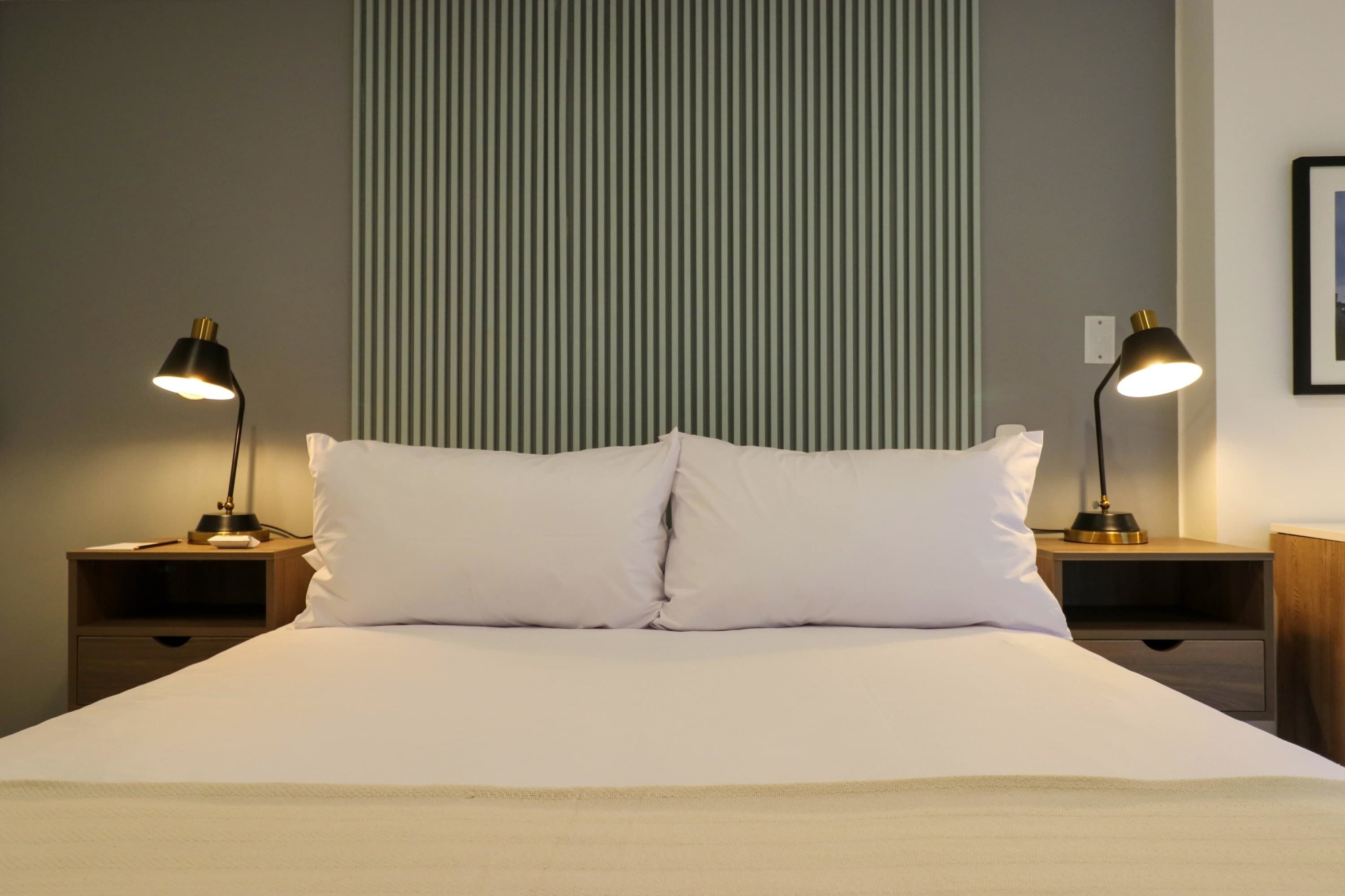 A neatly made bed with two bedside lamps, a striped wall, and a framed picture on the wall.