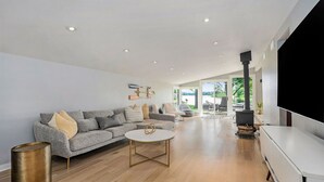 A spacious living room with a grey sofa, a round coffee table, and a large TV screen.