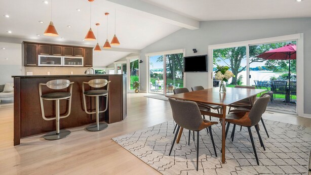 A modern kitchen with bar stools, a dining area with a table and chairs, and a view of the outdoors.