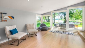 A modern living room with a wooden floor, two chairs, a sofa, and a large sliding glass door leading to an outdoor area.