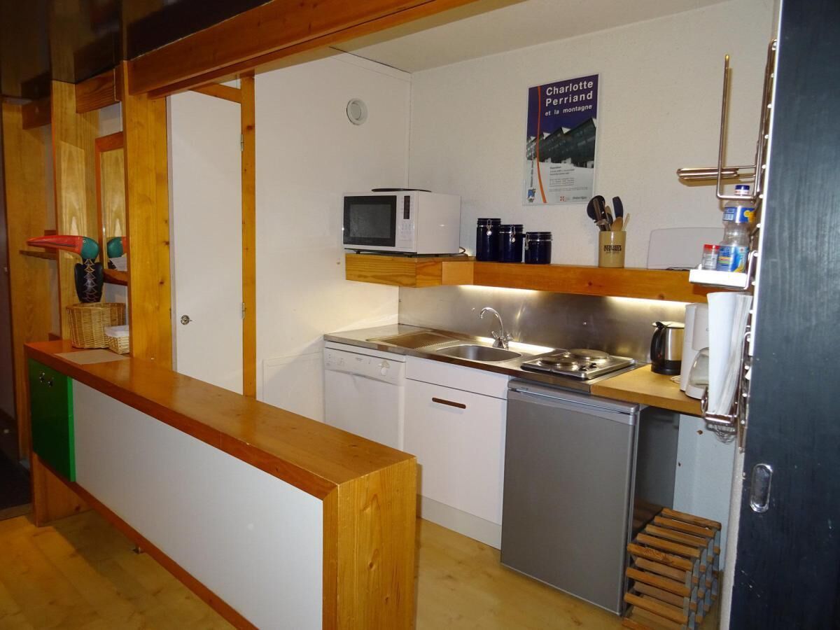 Cocina compacta con microondas, pileta y lavavajillas. Cuenta con un mostrador de madera y un refrigerador pequeño.
