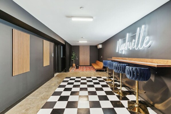 Un hall d’entrée moderne avec un sol à carreaux, un panneau lumineux au néon, un canapé et des tabourets de bar.