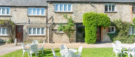 A stone building with a garden patio featuring white metal chairs and a table.