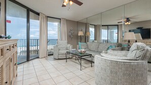 A spacious living room with a balcony, large windows, and a ceiling fan. - Beach Front 2 Bedroom Condo - Phoenix East 407 (Orange Beach)