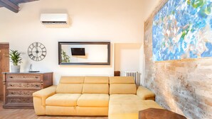 Un salon avec un canapé jaune, un meuble en bois, une horloge, un tableau encadré et une grande peinture abstraite accrochée au mur.