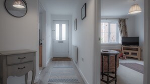 Een gang met een deur, een radiator, een tafeltje en een televisietoestel in een kamer.