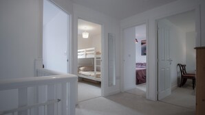 Een gang met een stapelbed, een houten stoel en een deur naar een andere kamer.