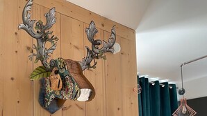 Ein Zimmer mit Holzwandverkleidung, einem aufgehängten Hirschgeweih als Dekoration, einem gerahmten Foto und einer hängenden Pendelleuchte.