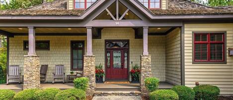 A two-story house with a front porch, stone pillars, and a red door.