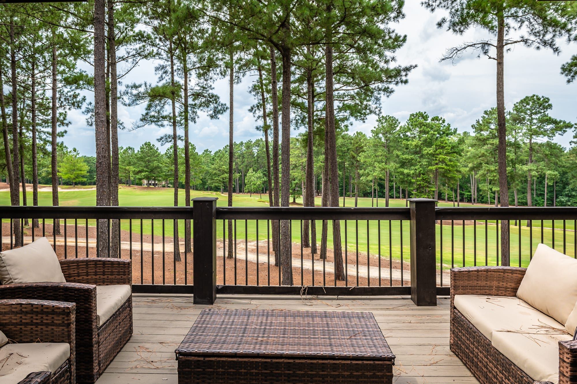 A covered outdoor area with wicker furniture and a view of a golf course.