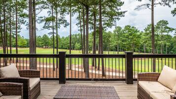 A covered outdoor area with wicker furniture and a view of a golf course.