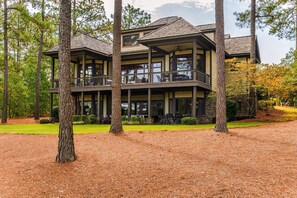 A multi-story house with a covered porch and a second level balcony, surrounded by trees and a well-maintained lawn.