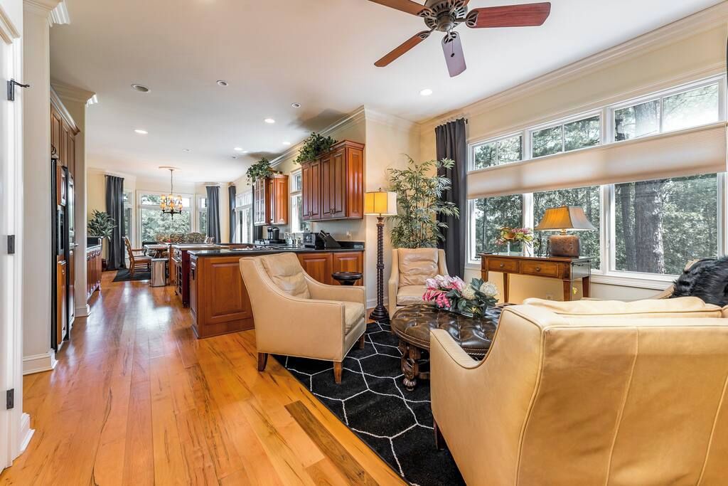 A spacious living area with a kitchen, wooden flooring, and large windows.