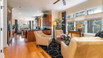 A spacious living area with a kitchen, wooden flooring, and large windows.