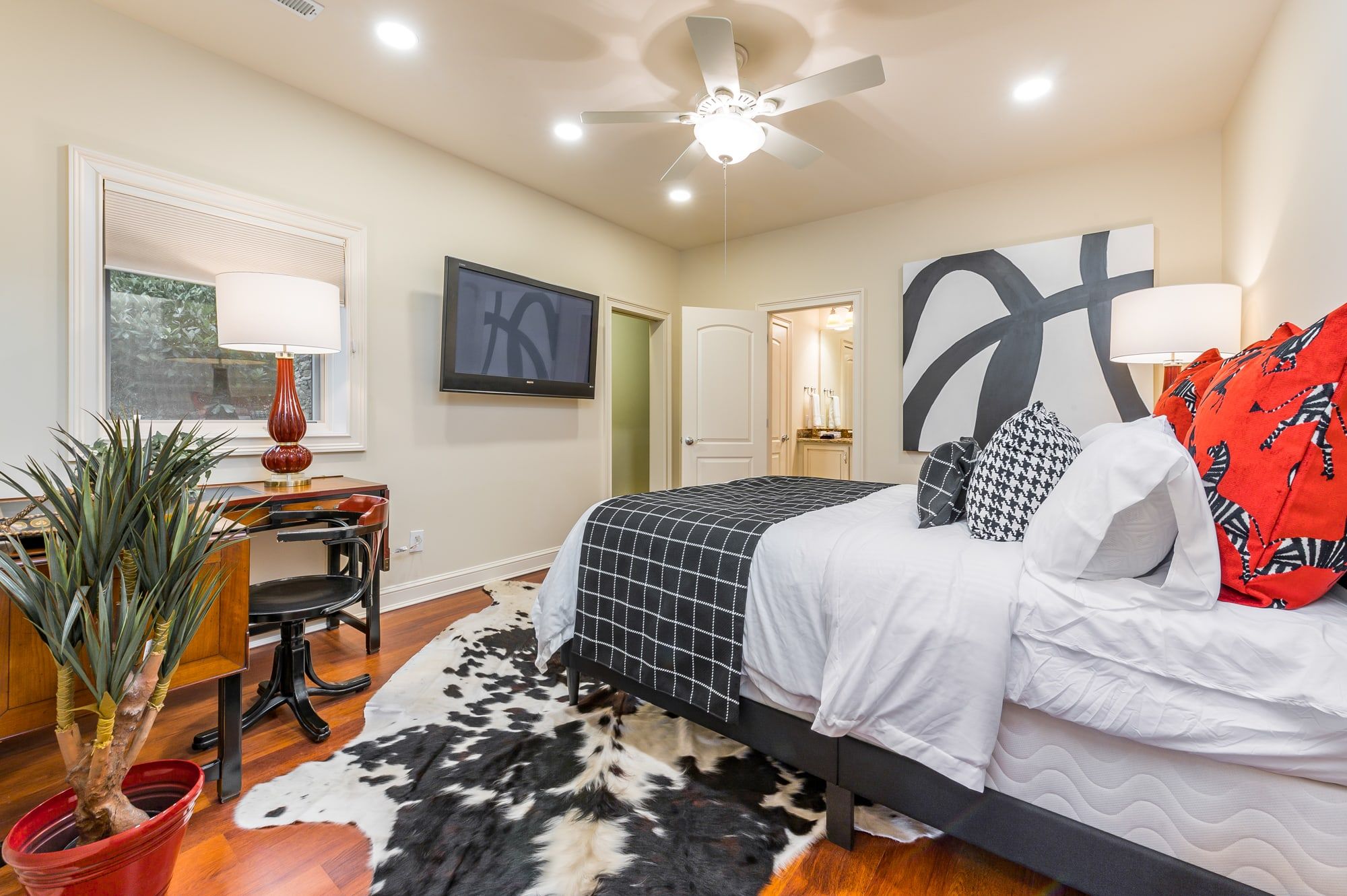 A bedroom with a bed, a desk, a television, and a ceiling fan.