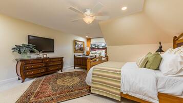 A bedroom with a bed, a wooden dresser, a TV, a ceiling fan, and a large window.