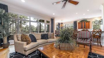 Un salon spacieux avec une table basse en bois, un canapé beige agrémenté de coussins à motifs et une grande fenêtre donnant sur la verdure.