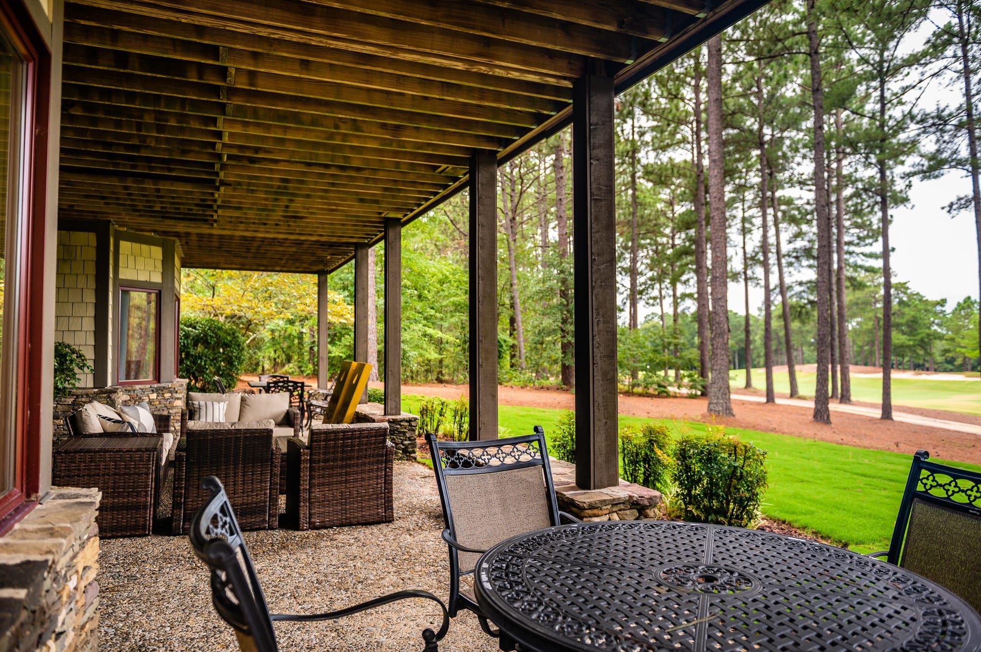 A covered patio with wicker furniture and a round table, overlooking a golf course.