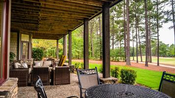 A covered patio with wicker furniture and a round table, overlooking a golf course.