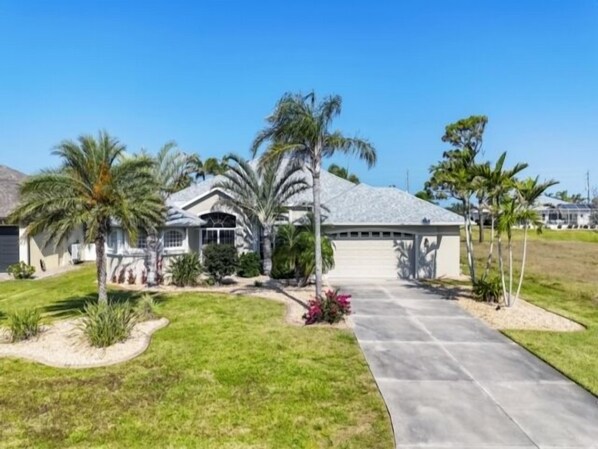 A single-story house with a covered driveway, surrounded by palm trees and a well-maintained lawn. - Beautiful Canal front home in Rotonda West (Rotonda West)
