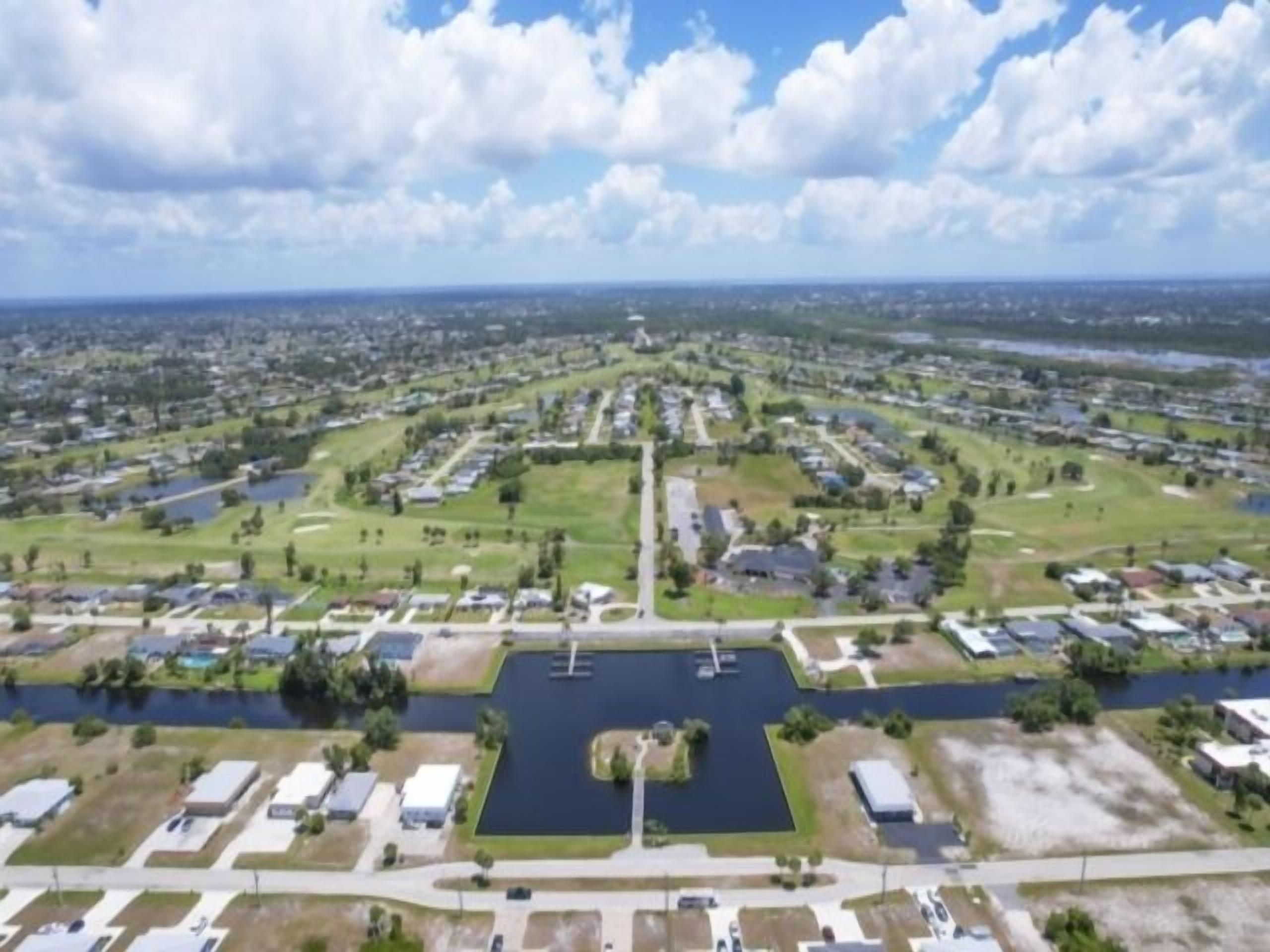 Vue aérienne d’un quartier résidentiel avec des maisons, un plan d’eau central et une route.
