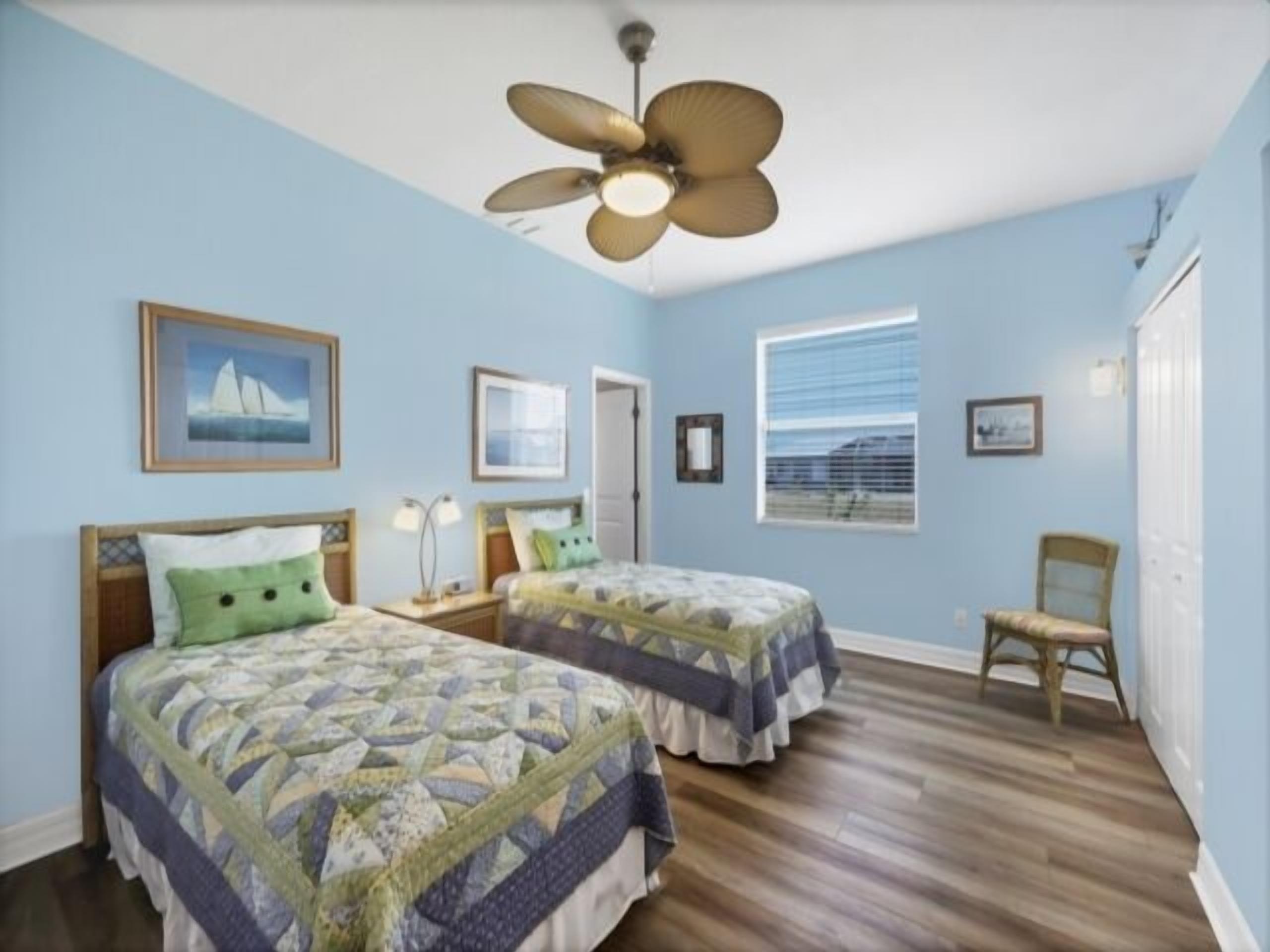 Une chambre avec deux lits, un ventilateur de plafond et une fenêtre.