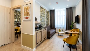 Quarto de hotel moderno com sofá, mesa de jantar, cadeiras, cozinha e uma janela grande com cortinas.