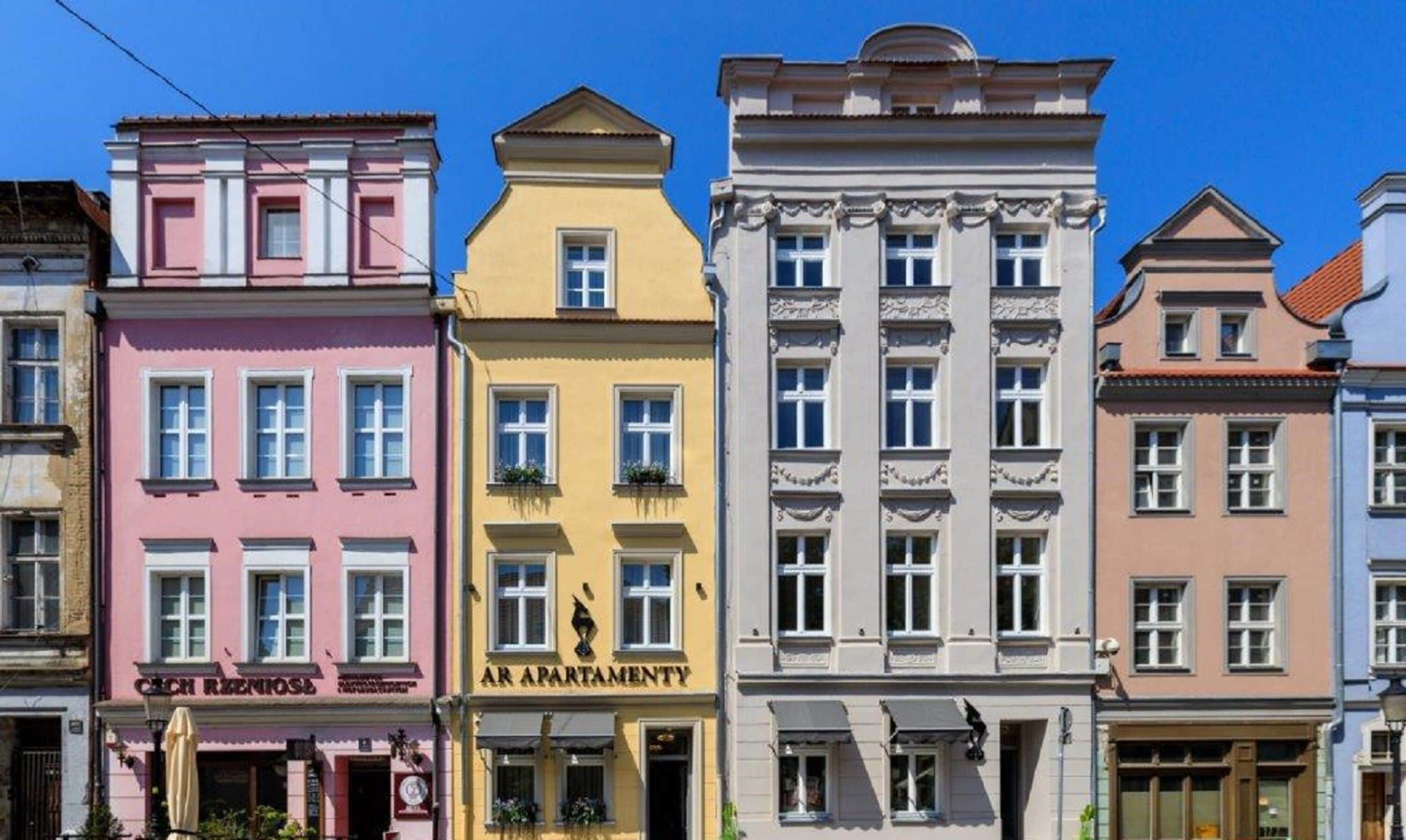 A row of colorful buildings with distinct architectural styles, including a pink building with a sign that reads "Czech Rzeszow" and a yellow building with a sign that reads "AR APARTMENTY".