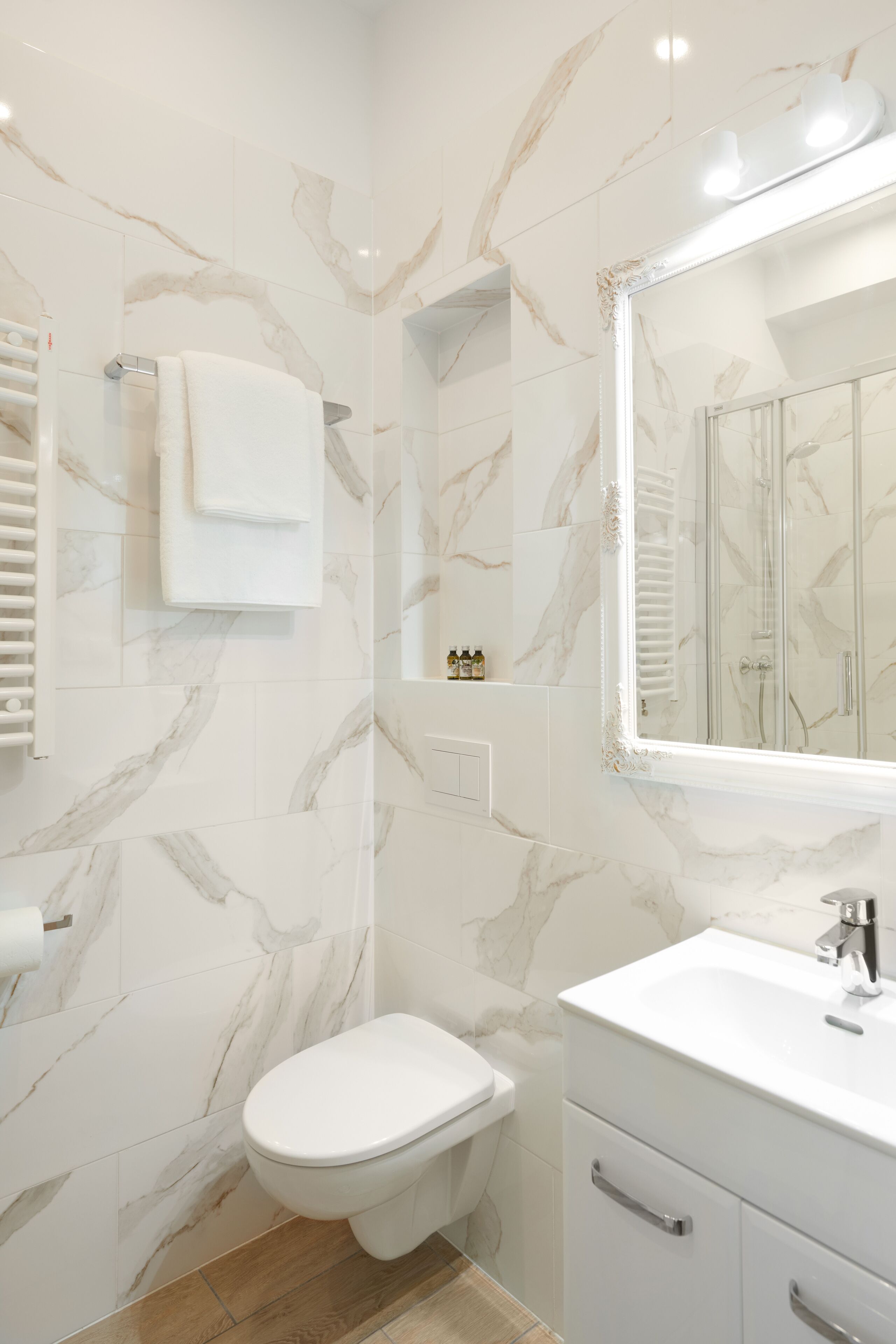 A modern bathroom with marble walls, a white toilet, a vanity with a mirror, and a shower enclosure.