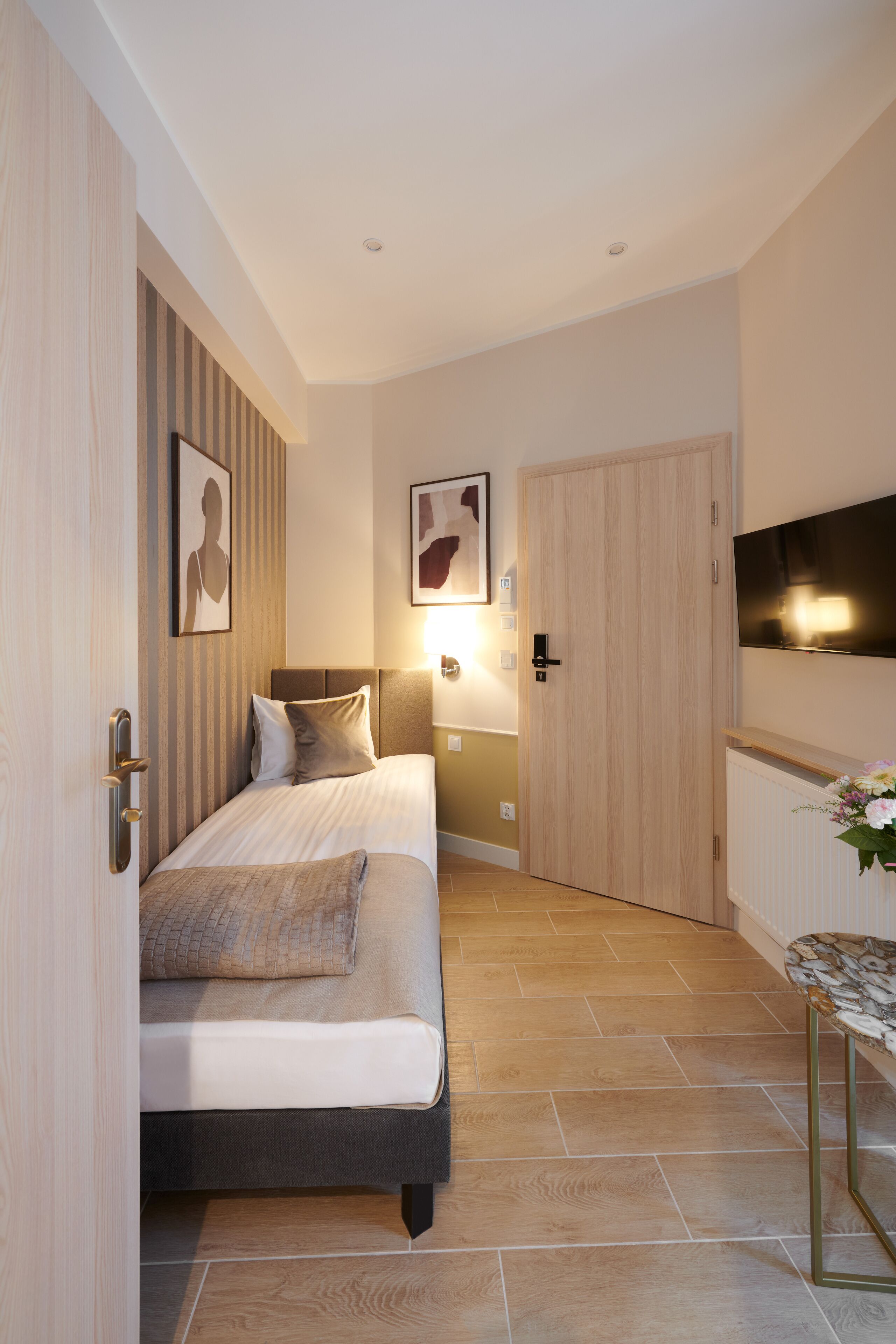 A modern hotel room with a bed, bedside table, and a TV mounted on the wall.