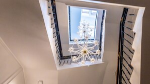 Uma escadaria moderna com claraboia, um candelabro e uma luminária decorativa no teto.
