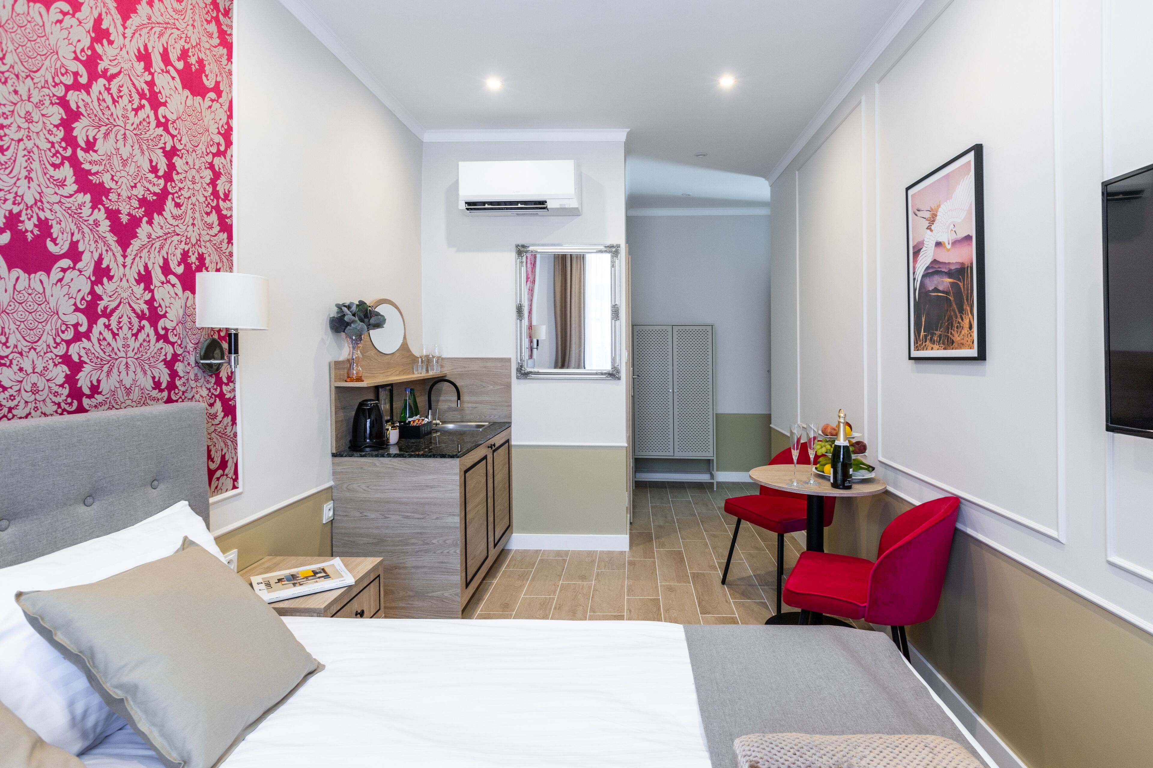 A hotel room with a bed, a desk, a chair, a small table, and a TV.