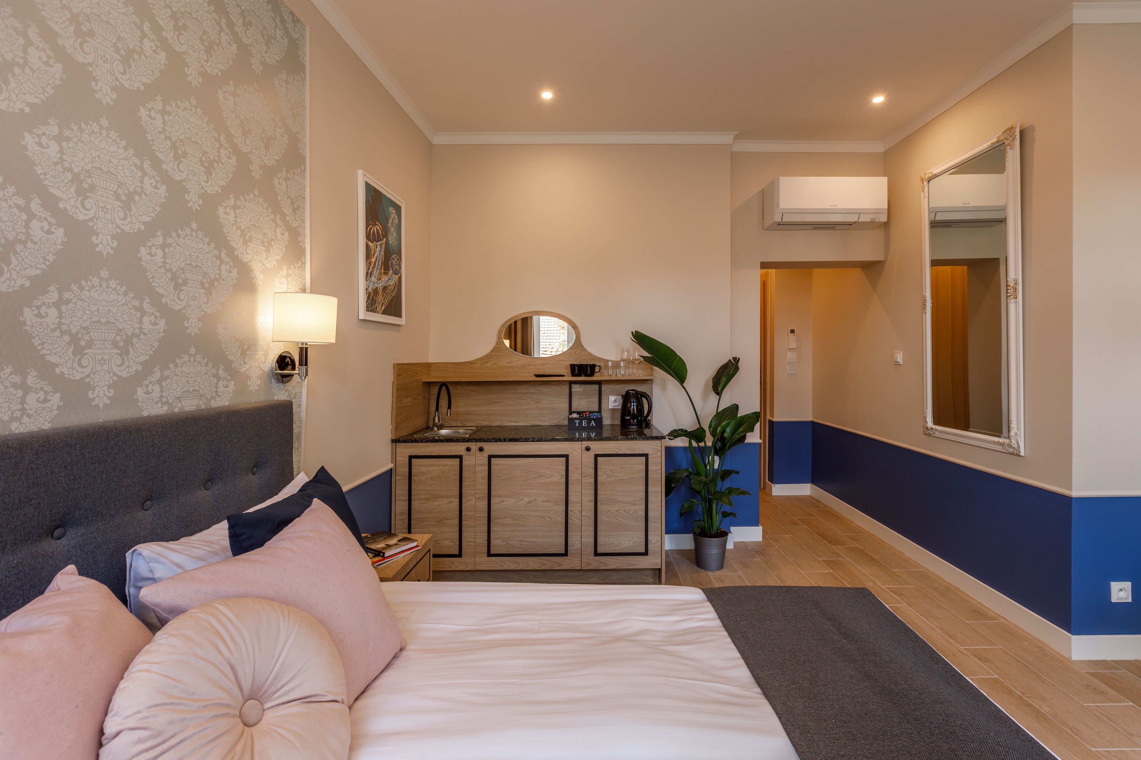 A bedroom with a bed, bedside table, lamp, and a view of a kitchen area.