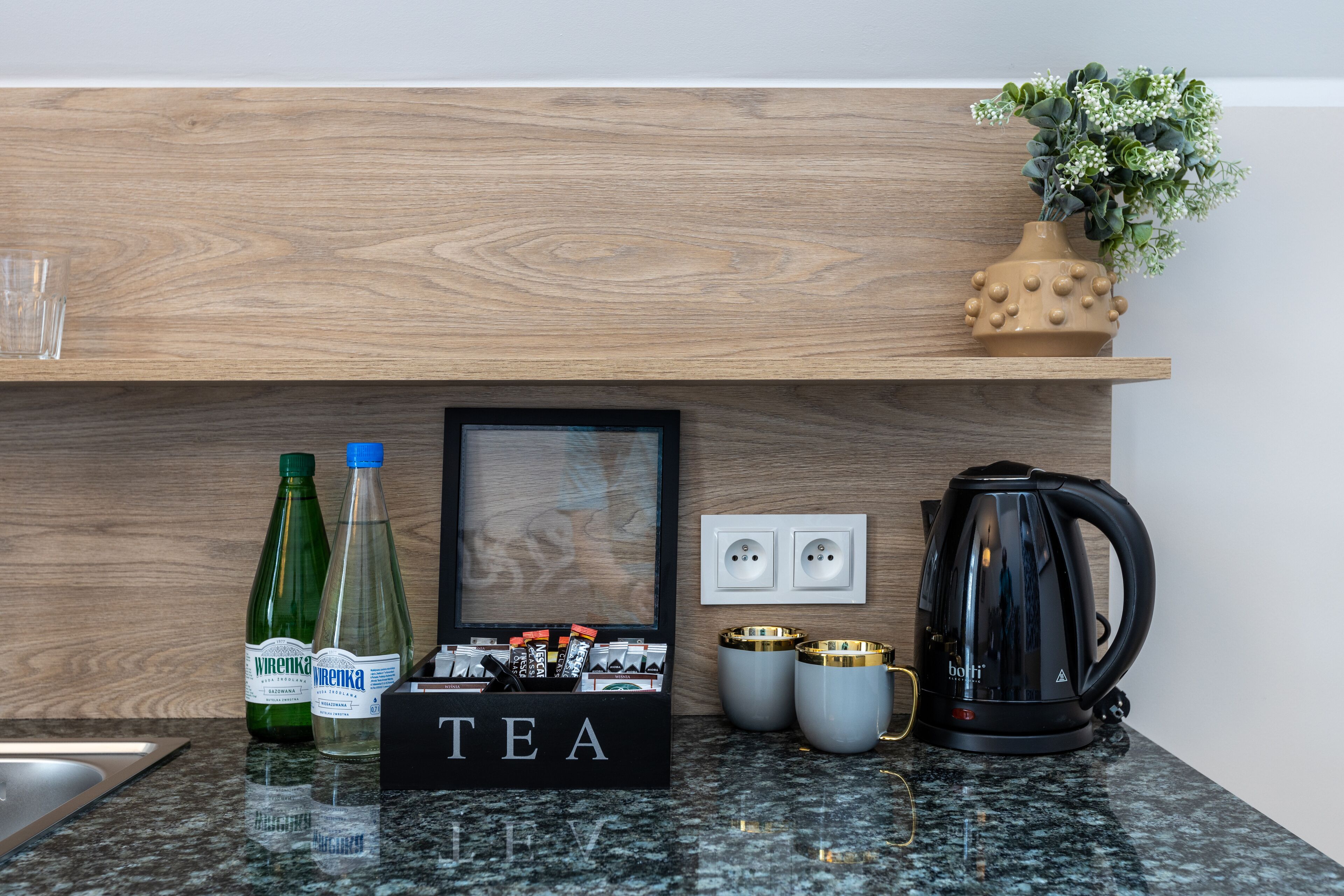 A kitchen counter with a tea station, two bottles of water, a framed picture, and a black kettle.