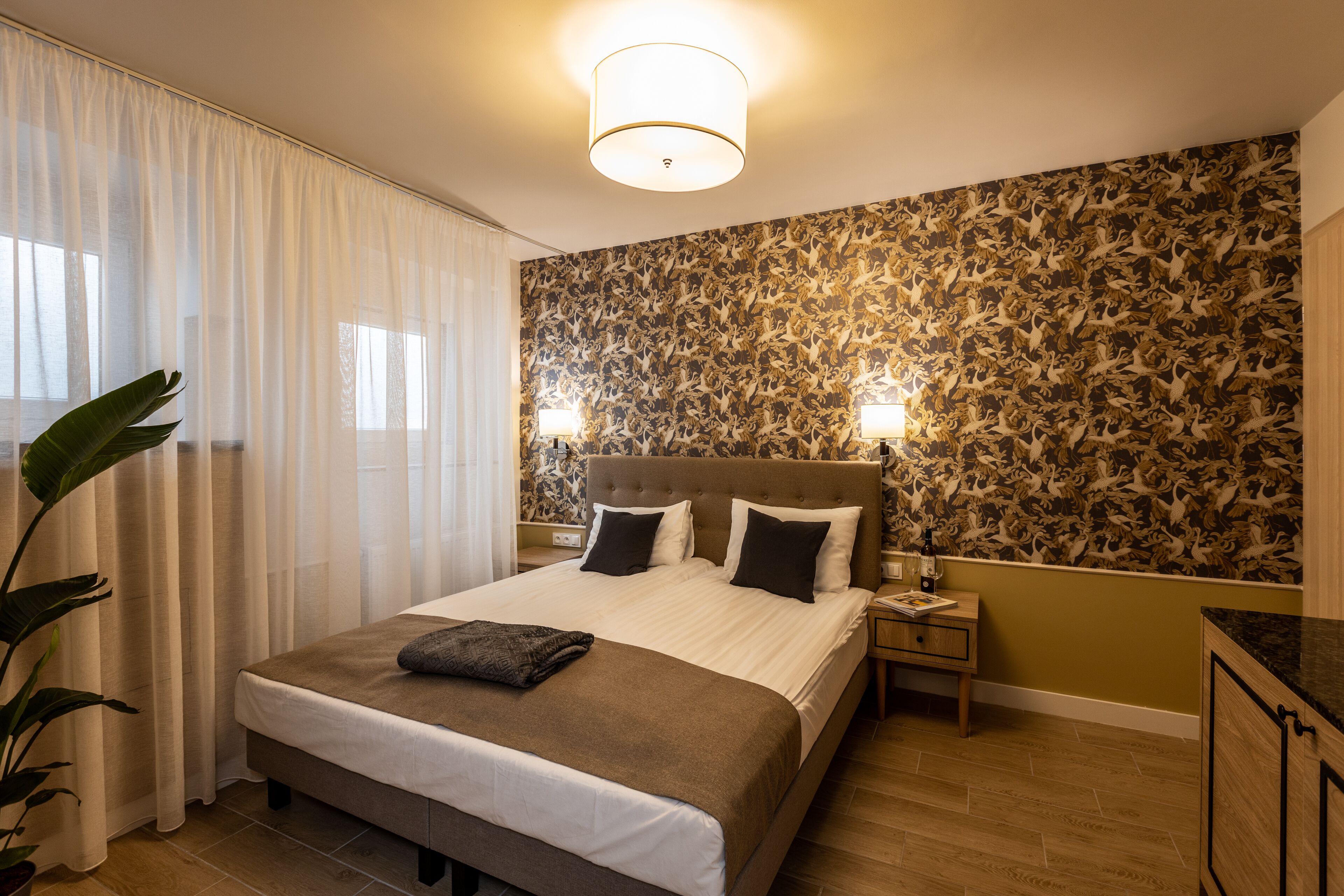 Ein Hotelzimmer mit einem großen Bett, zwei Nachttischlampen, einem Nachttisch, einer Zimmerpflanze und einer Wand mit Muster.