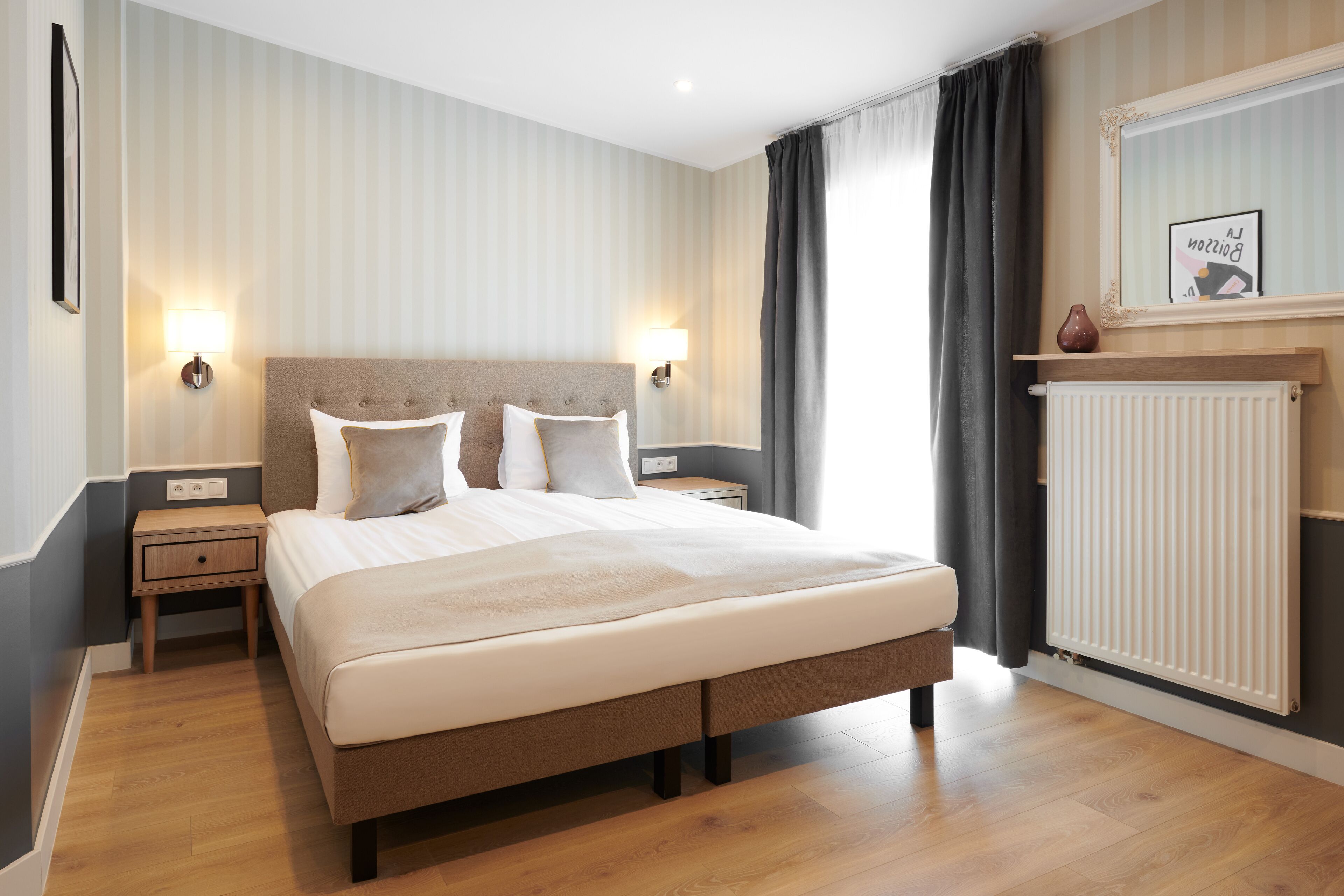 Une chambre bien rangée, avec un grand lit, des tables de chevet, un radiateur et un miroir au mur.
