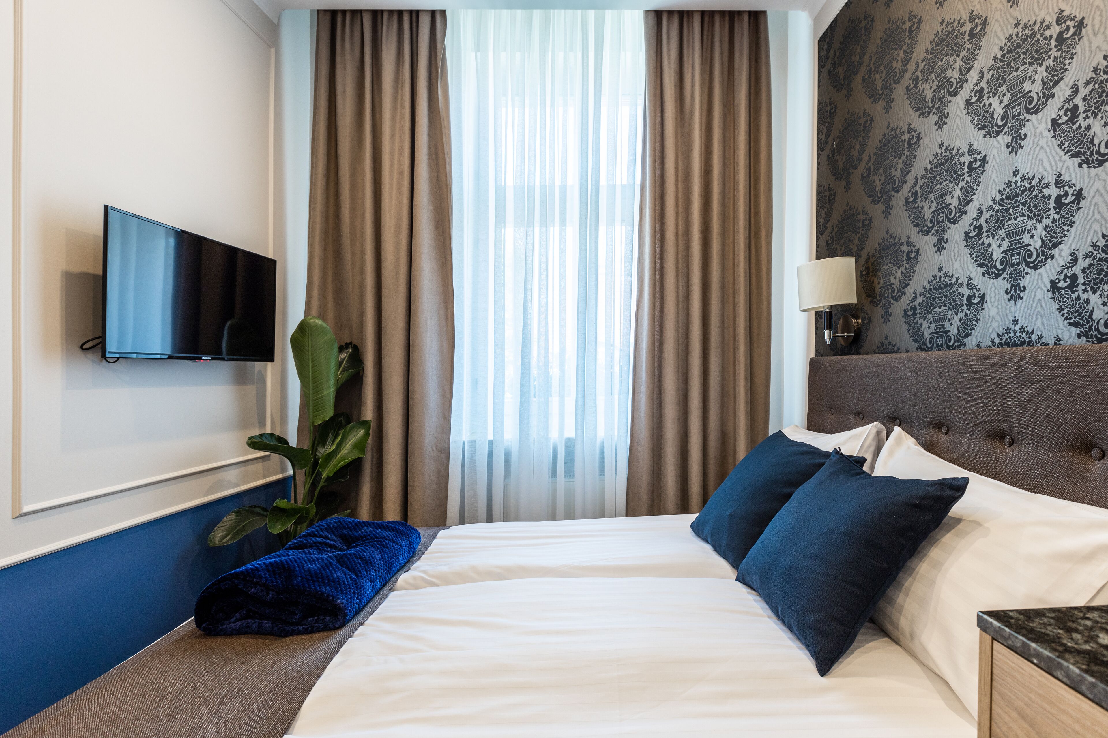 Ein Hotelzimmer mit Bett, Fernseher, Pflanze und einem Fenster mit Vorhängen.