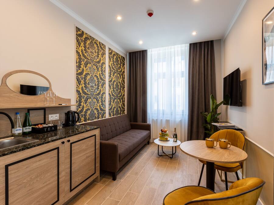 Um espaço de estar compacto com cozinha compacta, um sofá, área de jantar com cadeiras amarelas e uma grande janela com cortinas.
