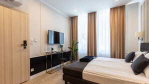 Quarto de hotel moderno com uma cama grande, uma escrivaninha com televisão de tela plana, um vaso de planta e vista para a cidade através de amplas janelas.