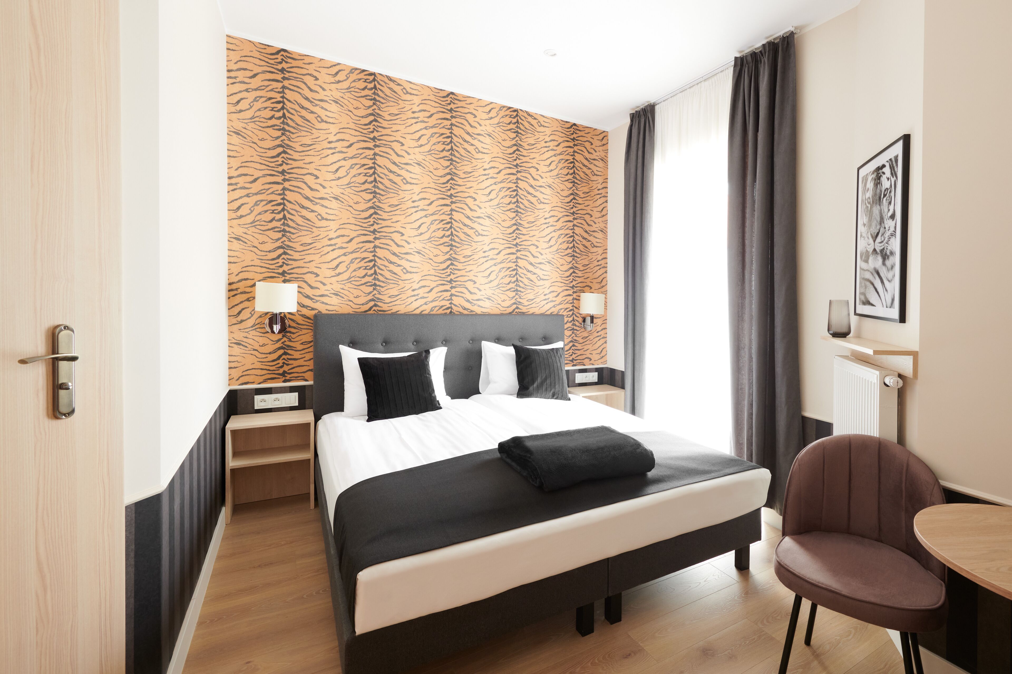 A hotel room with a bed, a chair, a table, and a tiger-striped wall.