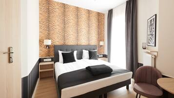 A hotel room with a bed, a chair, a table, and a tiger-striped wall.