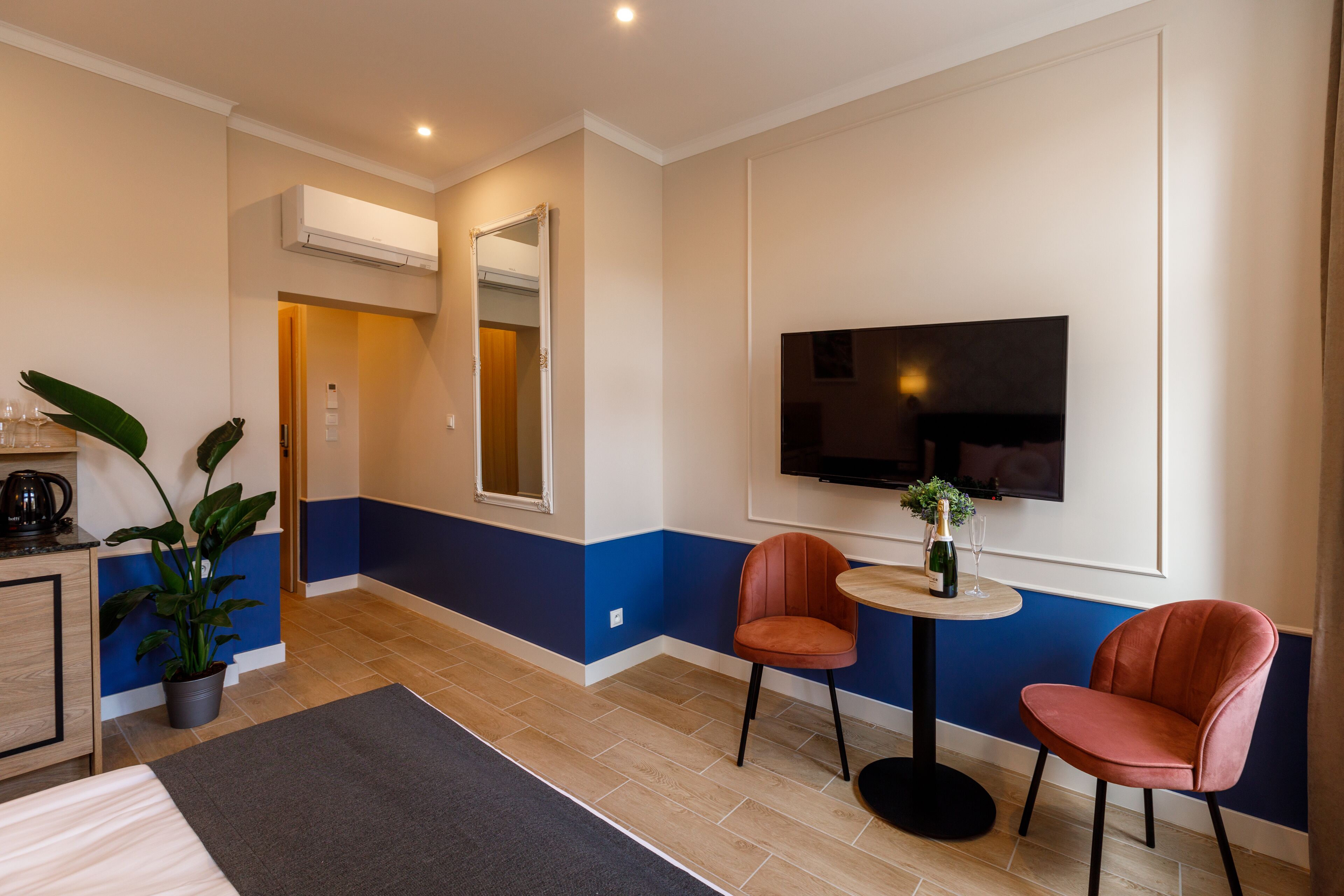 Une chambre d’hôtel comprenant un lit, un bureau, une chaise, une petite table avec une bouteille et des verres, et un téléviseur fixé au mur.