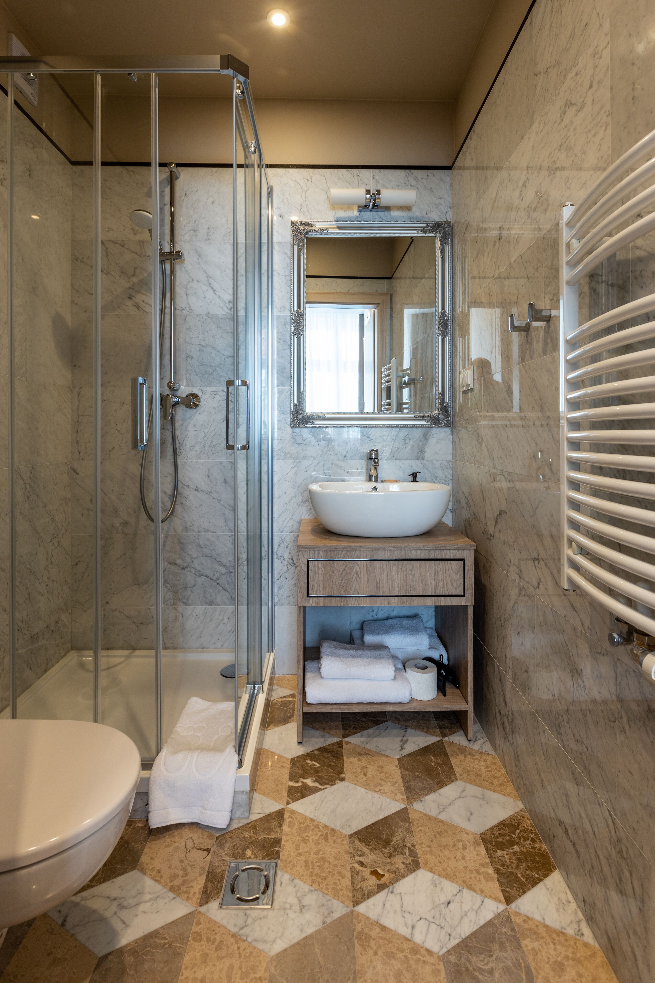 Un baño moderno con ducha de vidrio, lavamanos blanco y suelo de baldosas de mármol.