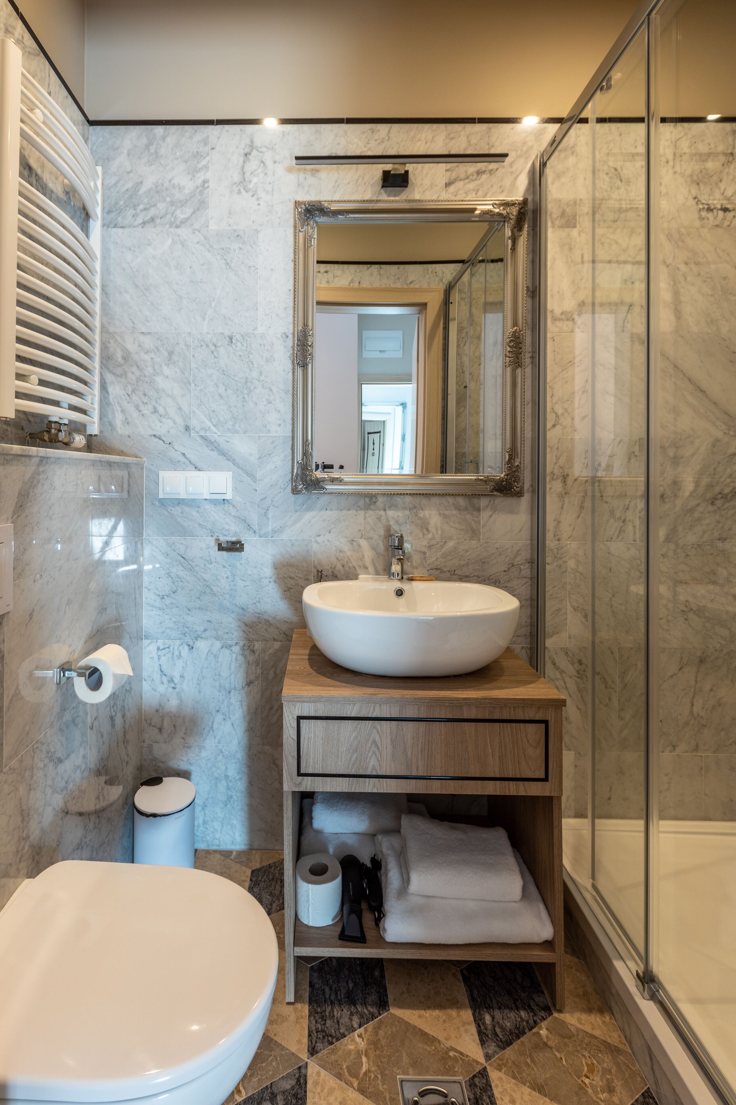 Un bagno moderno con un lavabo in marmo, un water, un box doccia in vetro e uno specchio sopra il lavabo.
